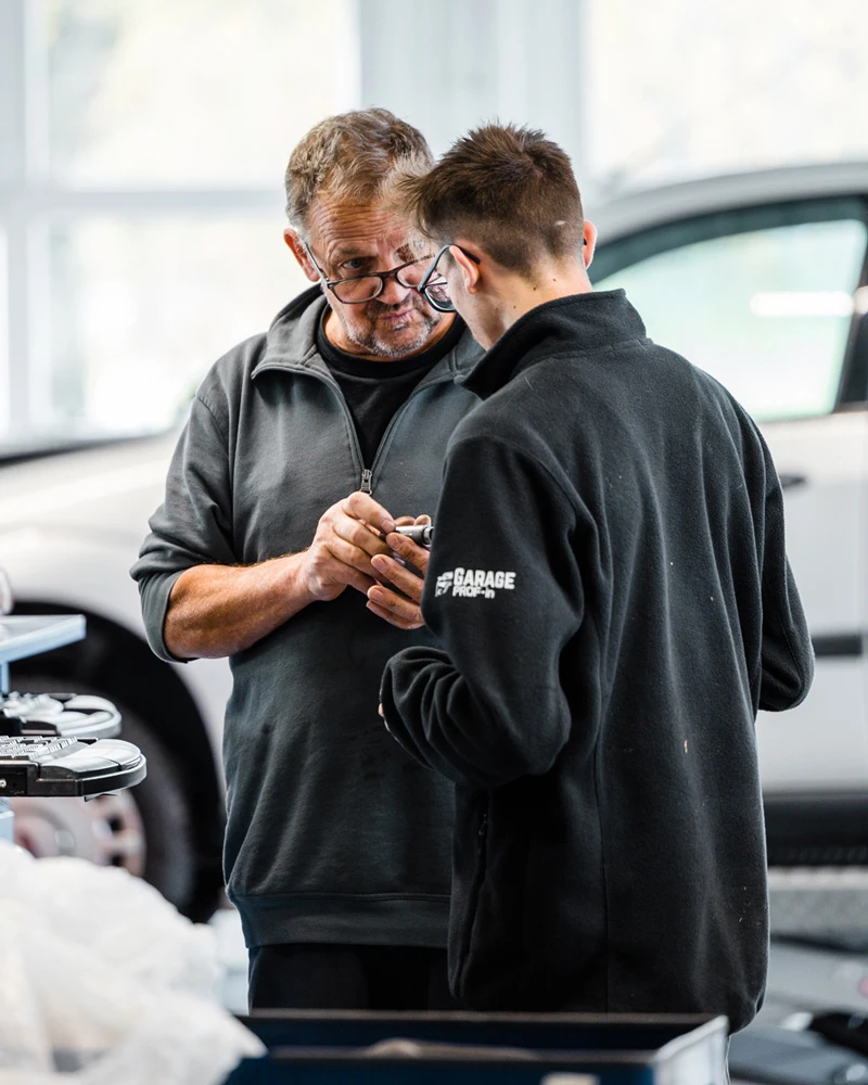 Maître d'apprentissage donnant des explications à son apprenti dans un garage automobile.