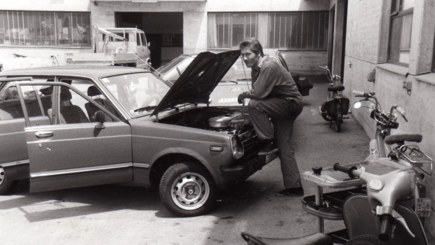 Photo d'archive noire et blanche d'un jeune appuyé sur une voiture.