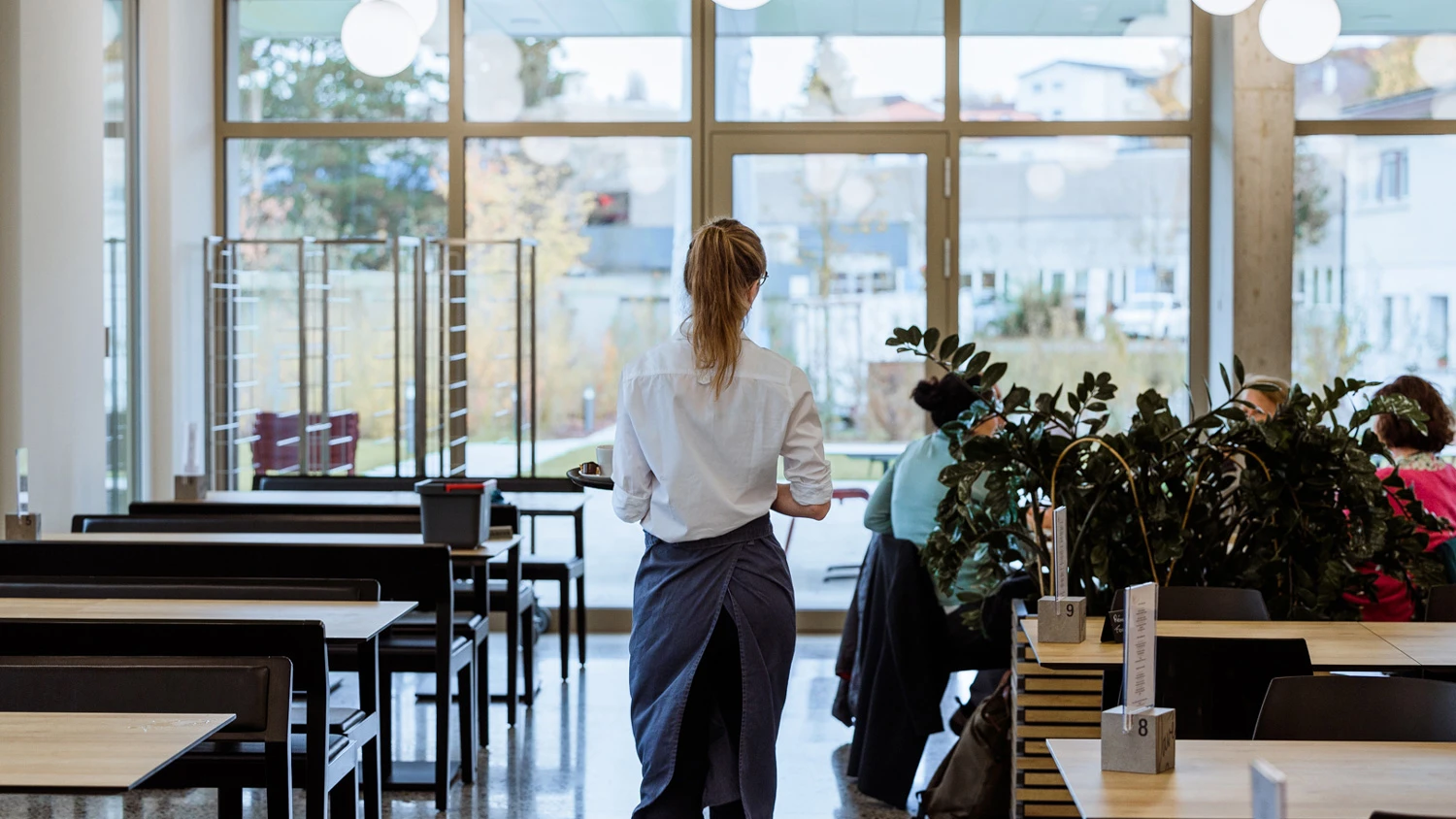 Jeune apprenti apportant des cafés à des clients dans un restaurant.