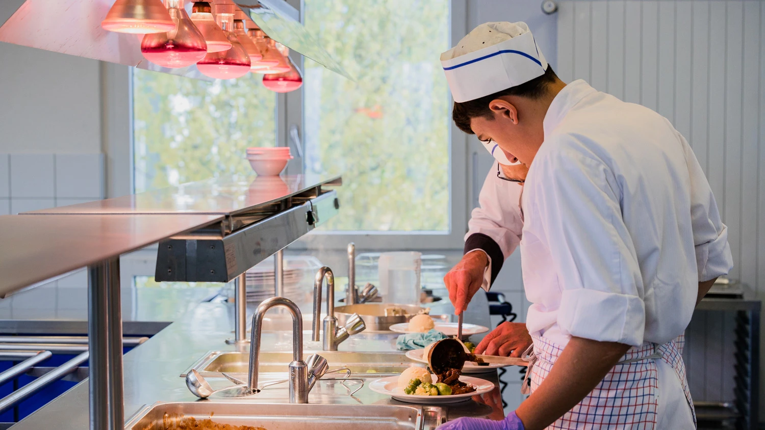 Jeune apprenti préparant une assiette dans une cuisine professionnelle.