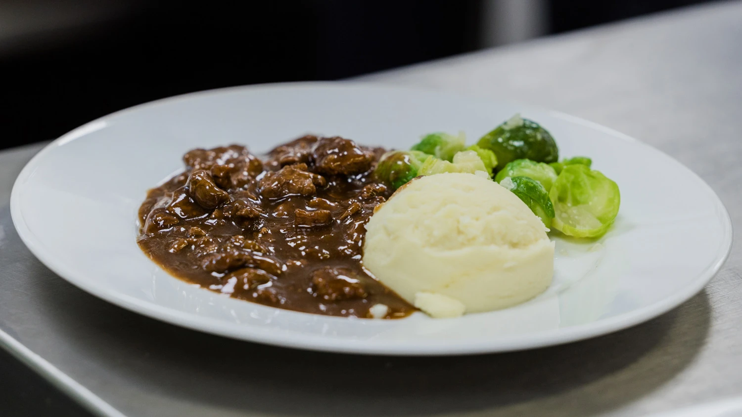 Assiette d'émincé de porc avec une sauce brune, des choux de Bruxelles et de la purée.