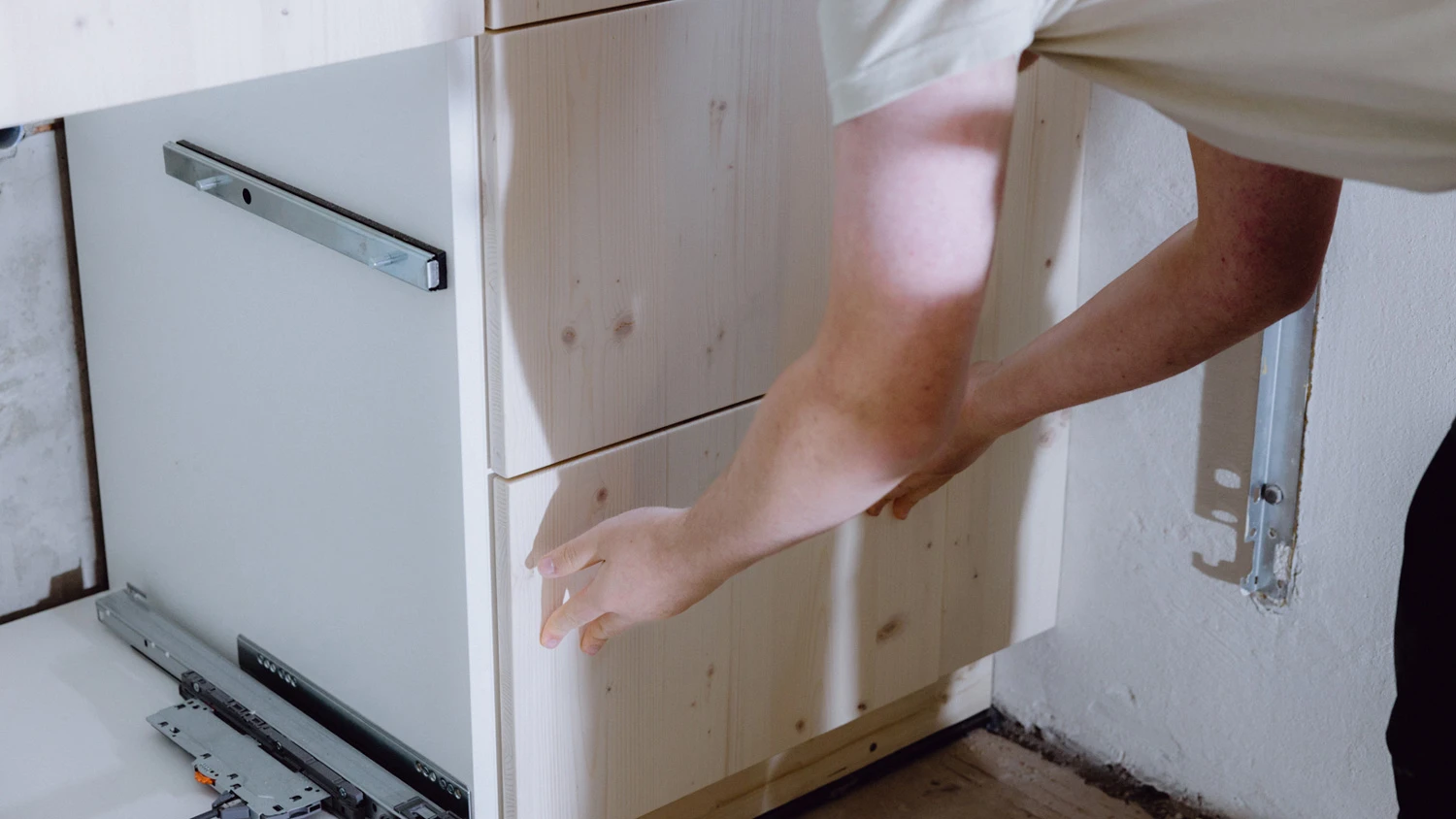 Jeune apprenti posant un tiroir en bois dans une cuisine en construction.