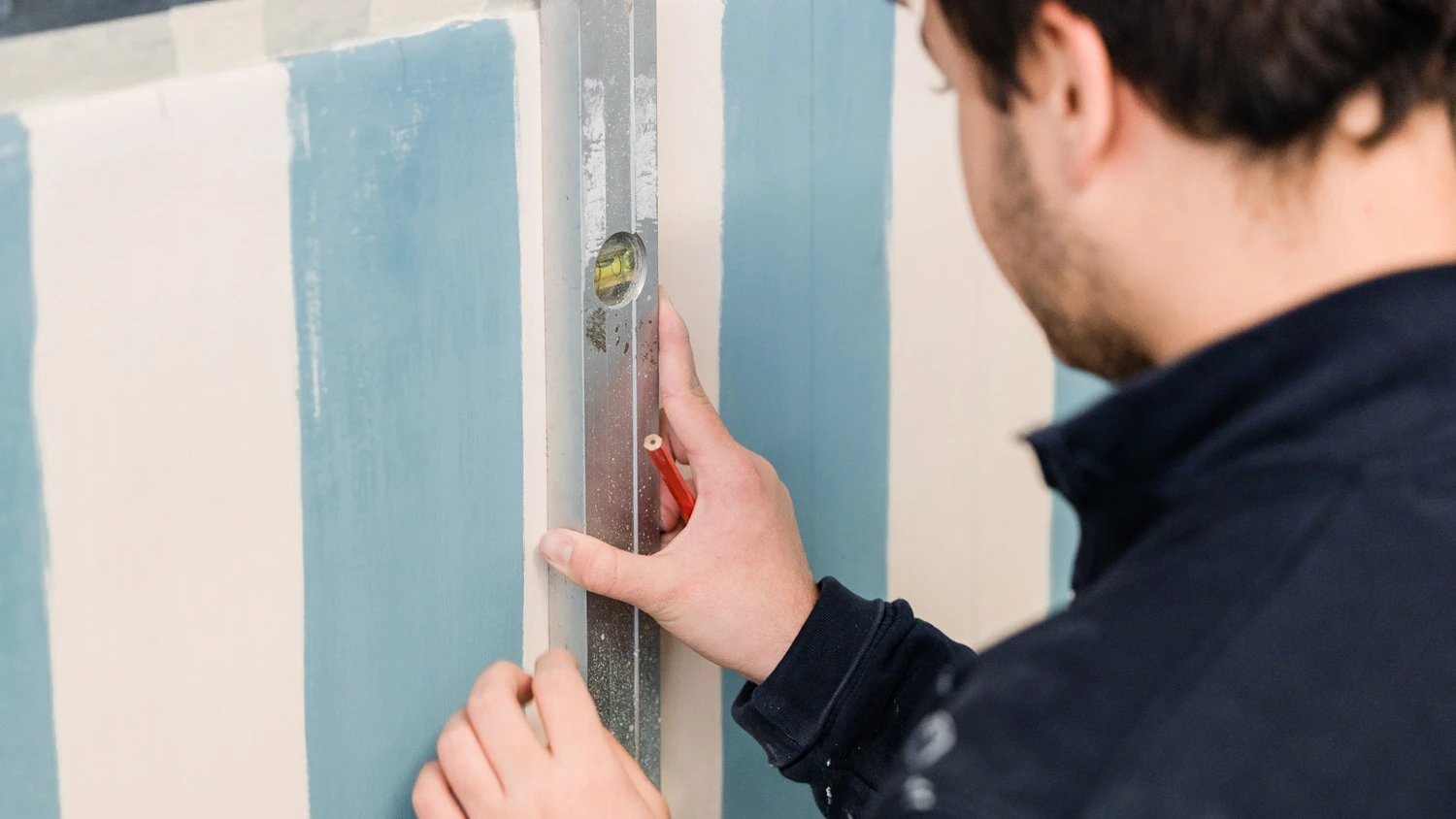 Jeune apprenti vérifiant le niveau d'une peinture sur un mur.