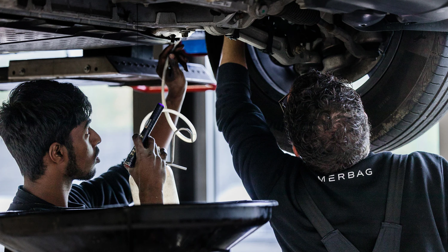 Junger Lehrling, der die Unterseite eines hochgelegten Autos repariert.