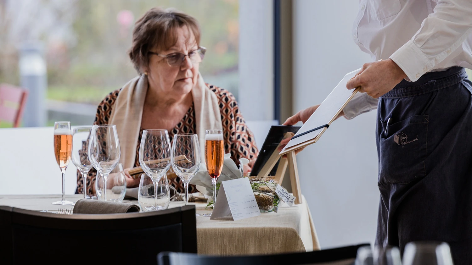 Jeune apprenti proposant la carte du restaurant à une cliente.